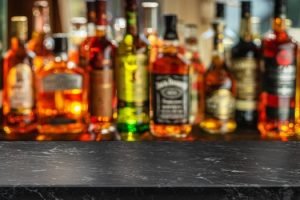 Beautiful bokeh from a row of alcoholic bottles in backlight and a marble gray counter table.